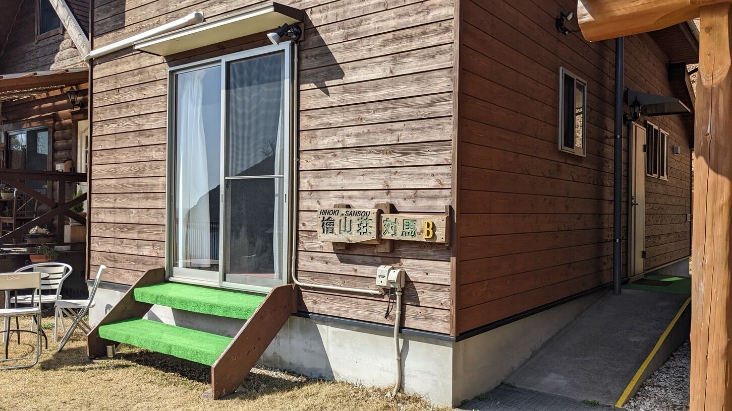 A wooden building with a sliding glass door, a small outdoor seating area, and a sign with Japanese characters.