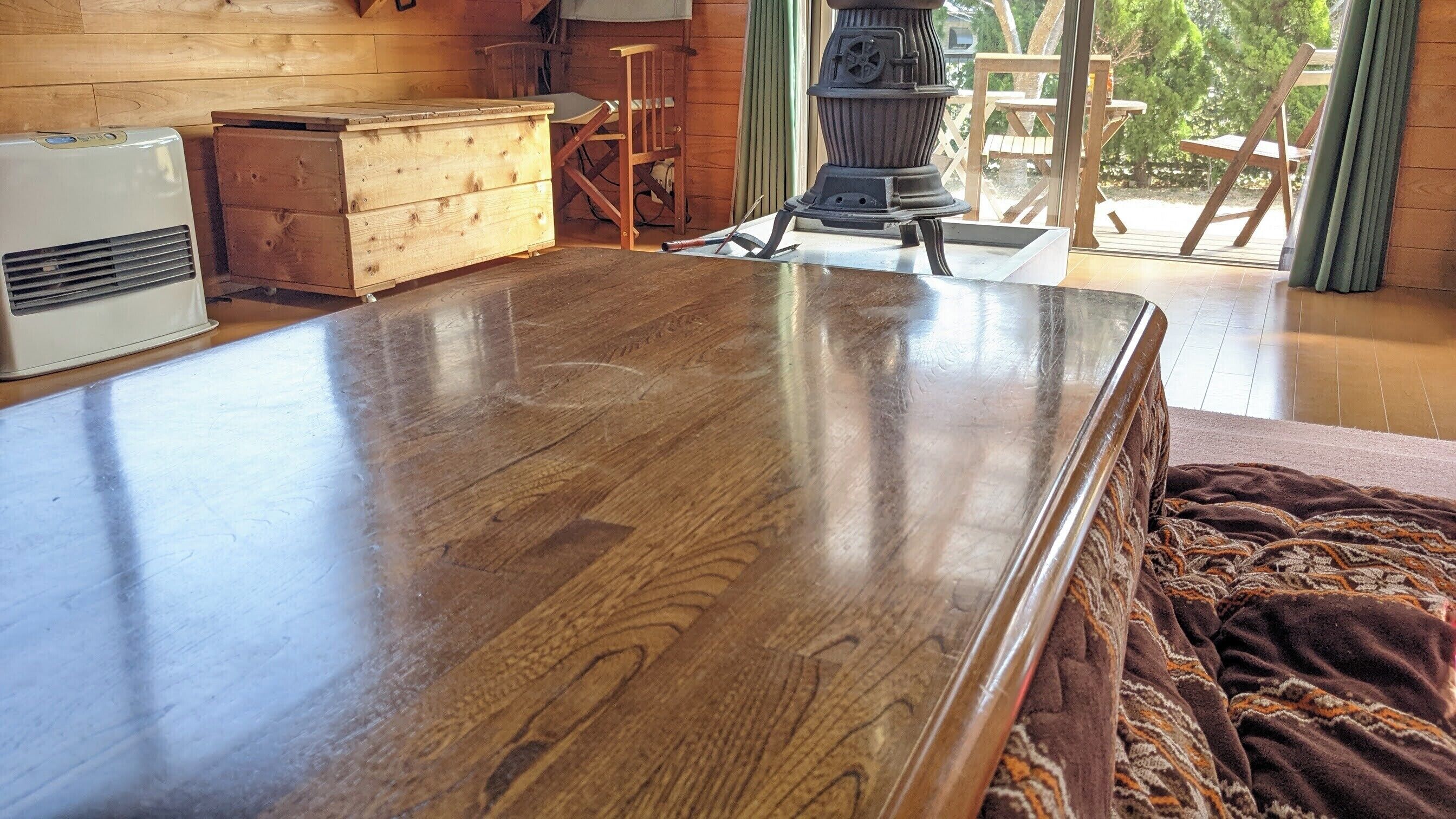 A wooden dining table in a room with a wooden chest, a heater, and a view of the outdoors.