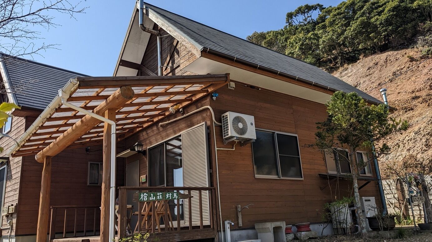 A wooden building with a covered porch, an air conditioning unit, and a sign with Japanese characters.