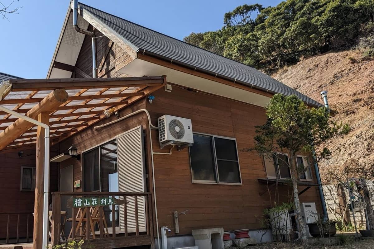 Un edificio de madera con un porche cubierto, un equipo de aire acondicionado y un letrero con caracteres japoneses.