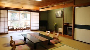 Tatami-mattoilla päällystetty huone, jossa on matala pöytä, tuoleja, televisio ja liukuovi.