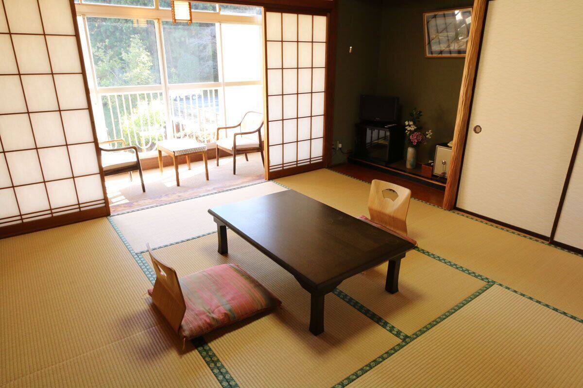 A tatami mat room with a low table and cushions, a sliding door, and a view of the outdoors.