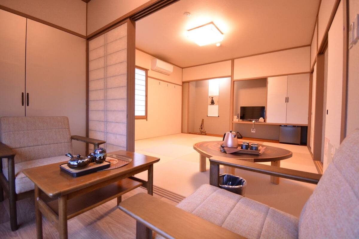 Een traditionele Japanse kamer met tatami vloerbedekking, een lage tafel met theeservies, een bank en schuifdeuren.