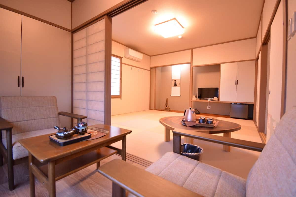A traditional Japanese-style room with tatami flooring, a low table with a tea set, a sofa, and sliding doors.