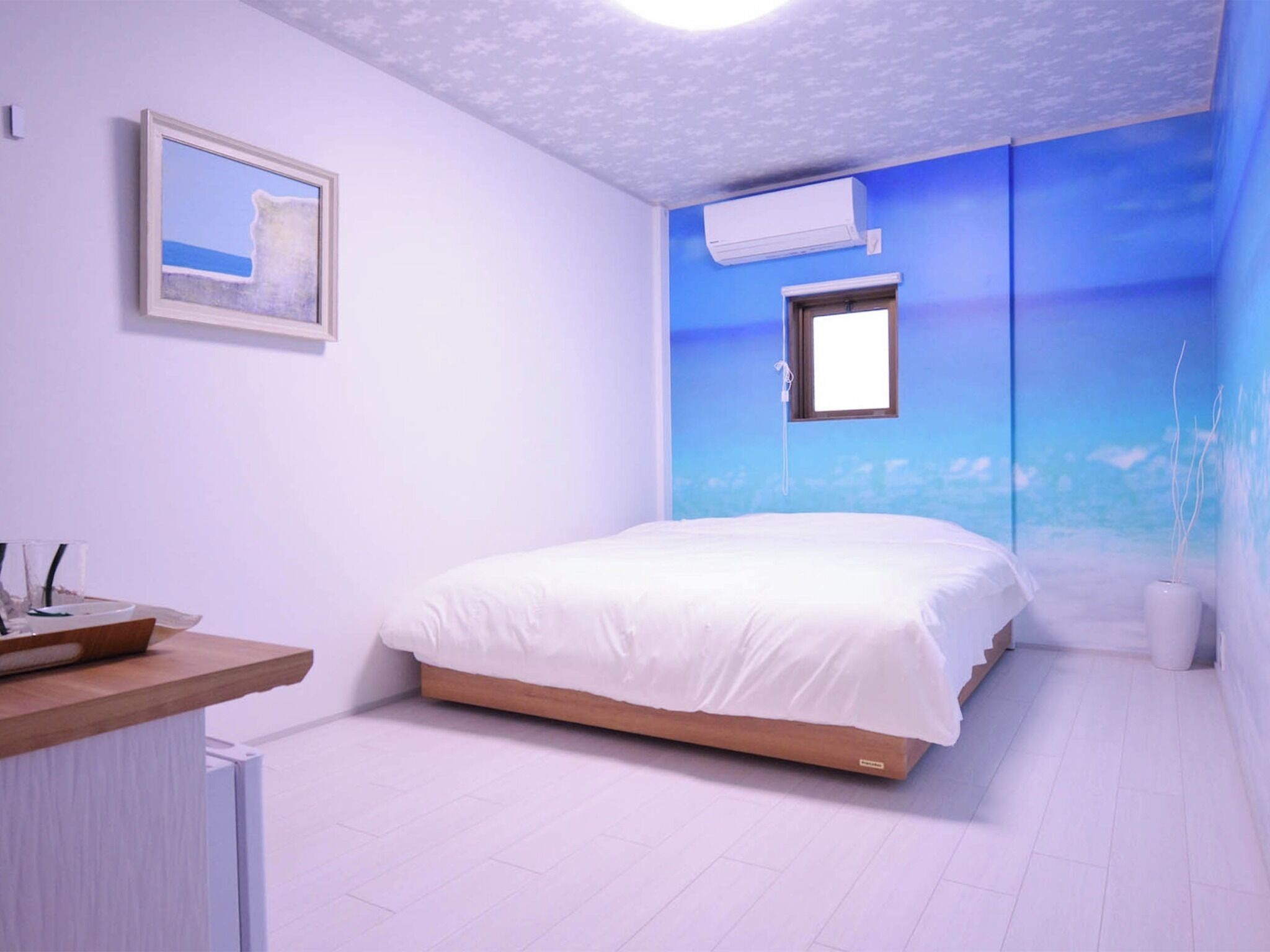 A bedroom with a bed, a nightstand, an air conditioning unit, and a wall mural.