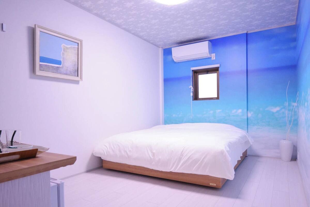 Een slaapkamer met een bed, nachtkastje, airconditioning en een muurschildering.