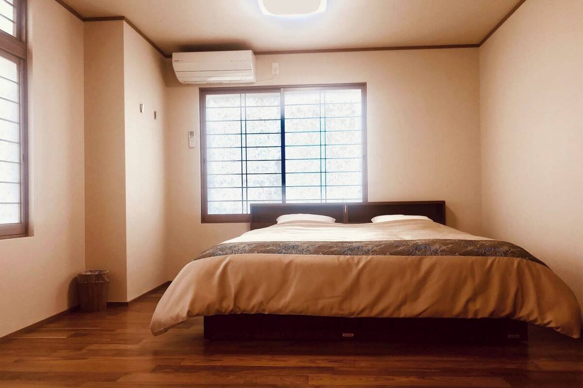 Een slaapkamer met een bed, een raam met zonwering, een airconditioning en een houten vloer.