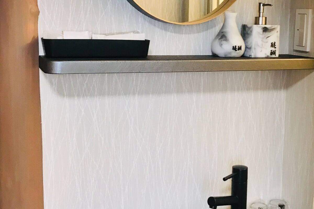 Een badkamer met een ronde spiegel, een zwarte wastafel en een plank met een zeepdispenser en een vaas.