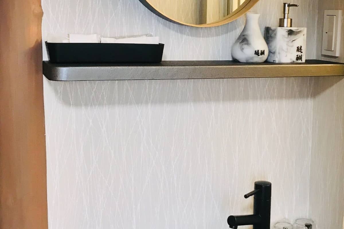 A bathroom with a round mirror, a black sink, and a shelf with a soap dispenser and a vase.