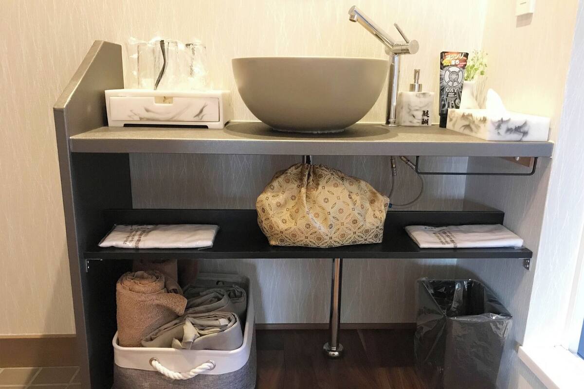 Een badkamer met een groot wastafelbakje, een handdoekrek, een prullenbak en een opbergbak met handdoeken.