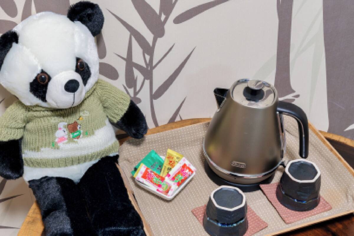 Een zacht panda-knuffel, een theepot en twee kopjes op een dienblad.