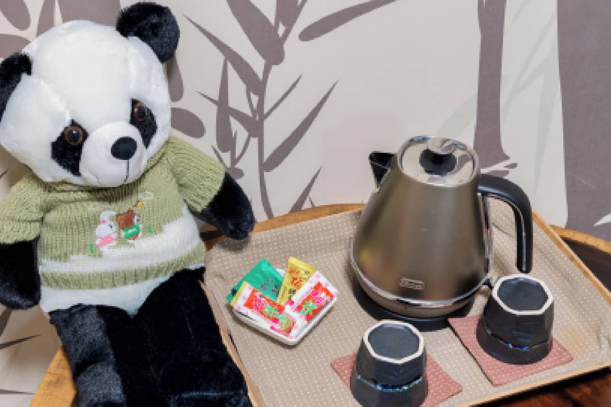 A plush panda toy, a teapot, and two cups on a tray.