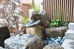 Ein Felsengarten mit Wasserspiel, umgeben von großen Steinen und Pflanzen.