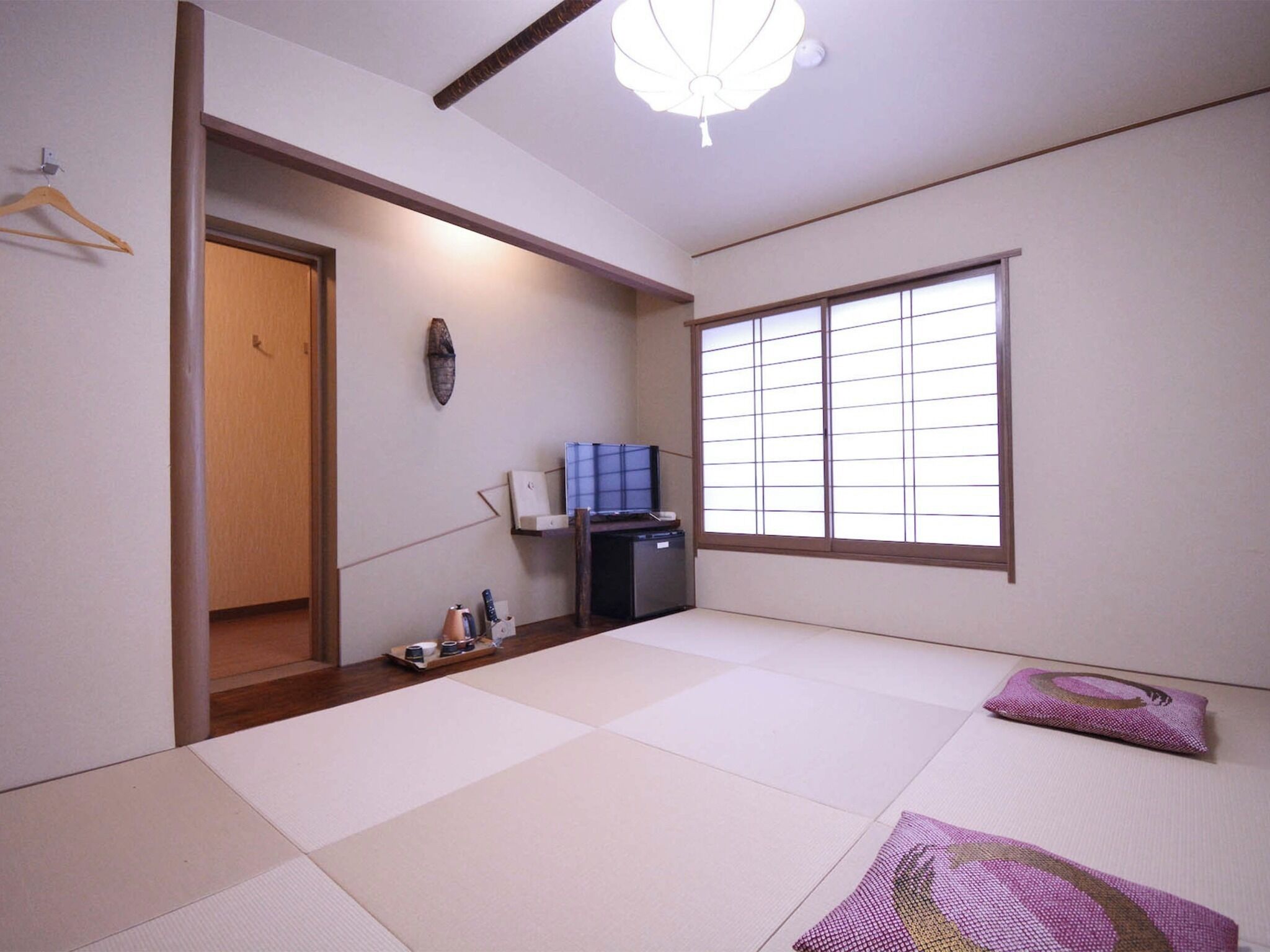 A traditional Japanese room with tatami flooring, a sliding door, a television, and a ceiling fan.