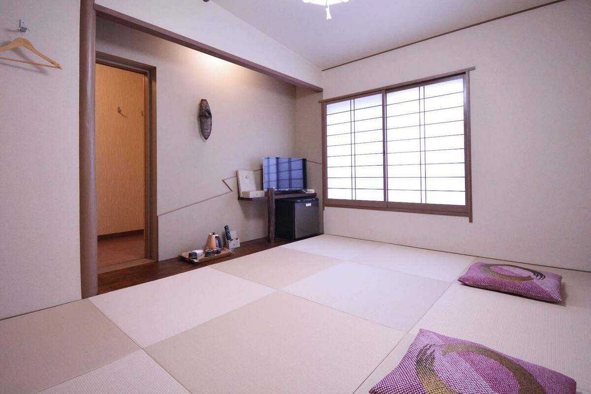 Een traditionele Japanse kamer met tatami vloerbedekking, een schuifdeur, een televisie en een plafondventilator.