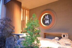 Ein traditionelles japanisches Gebäude mit Holzbeschichtung, einem Steingarten mit Teich und einer runden Mauer mit japanischen Schriftzeichen.