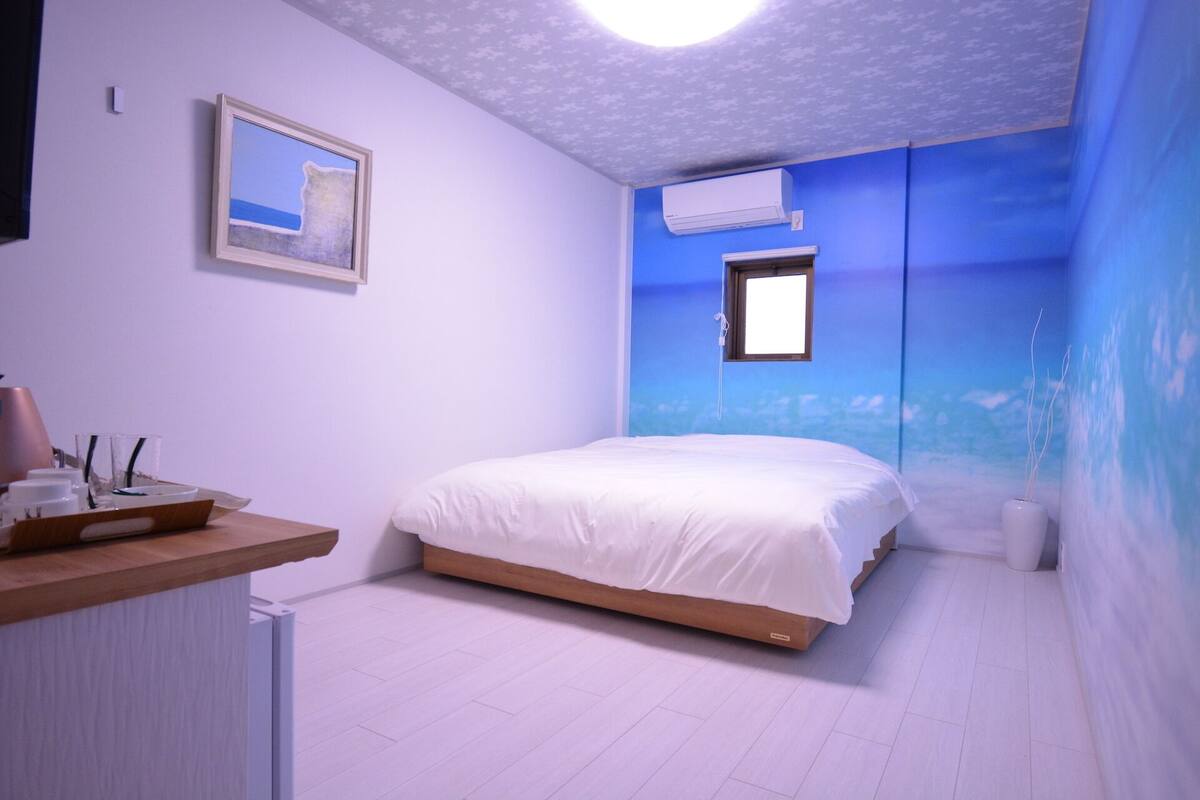 Een slaapkamer met een bed, een raam, een airconditioning en een aan de muur hangend schilderij.