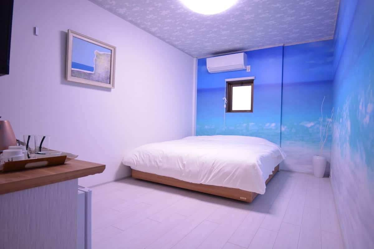 A bedroom with a bed, a window, an air conditioning unit, and a wall-mounted picture.