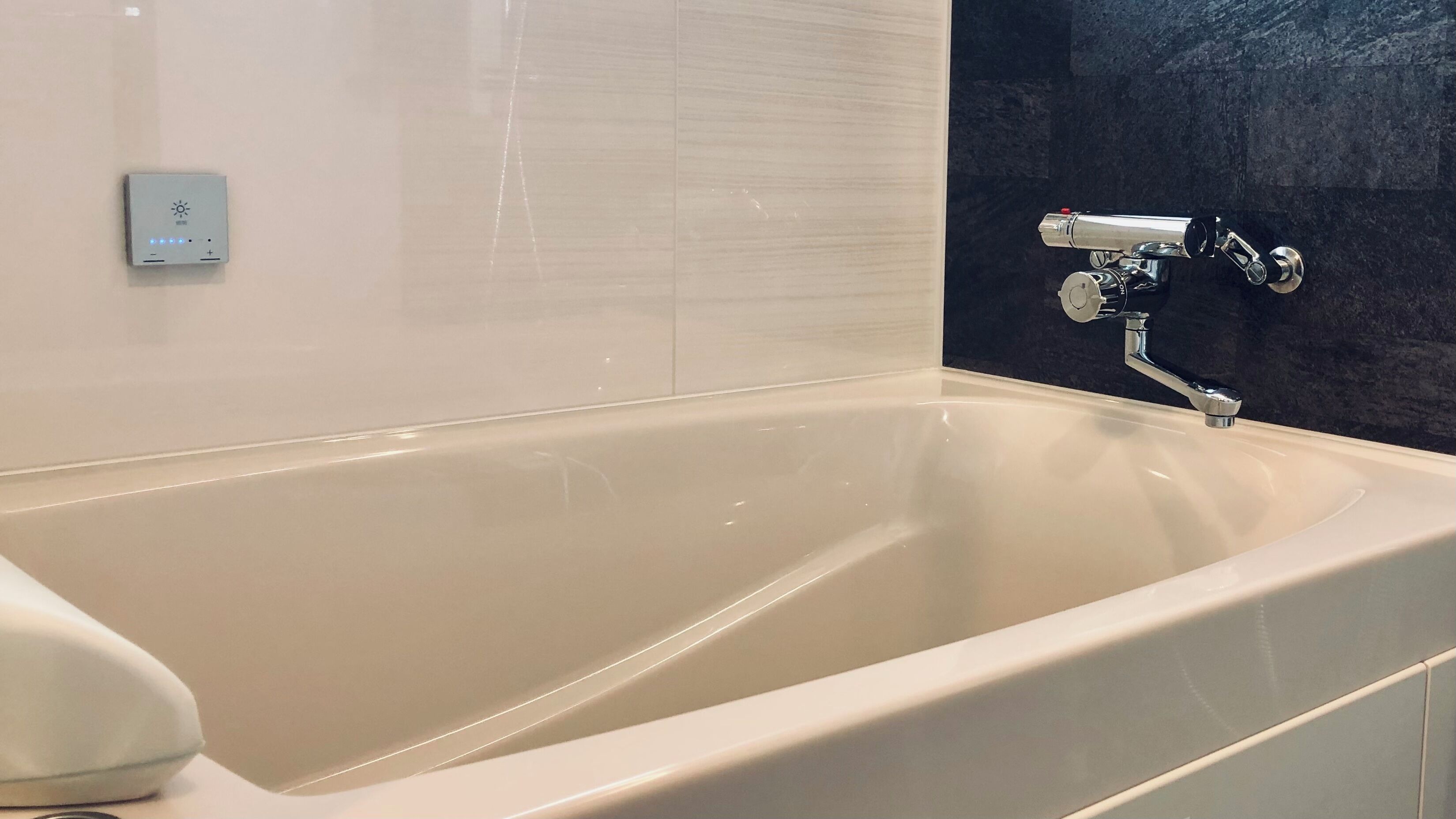 A modern bathroom with a bathtub, a wall-mounted control panel, and a dark textured wall.