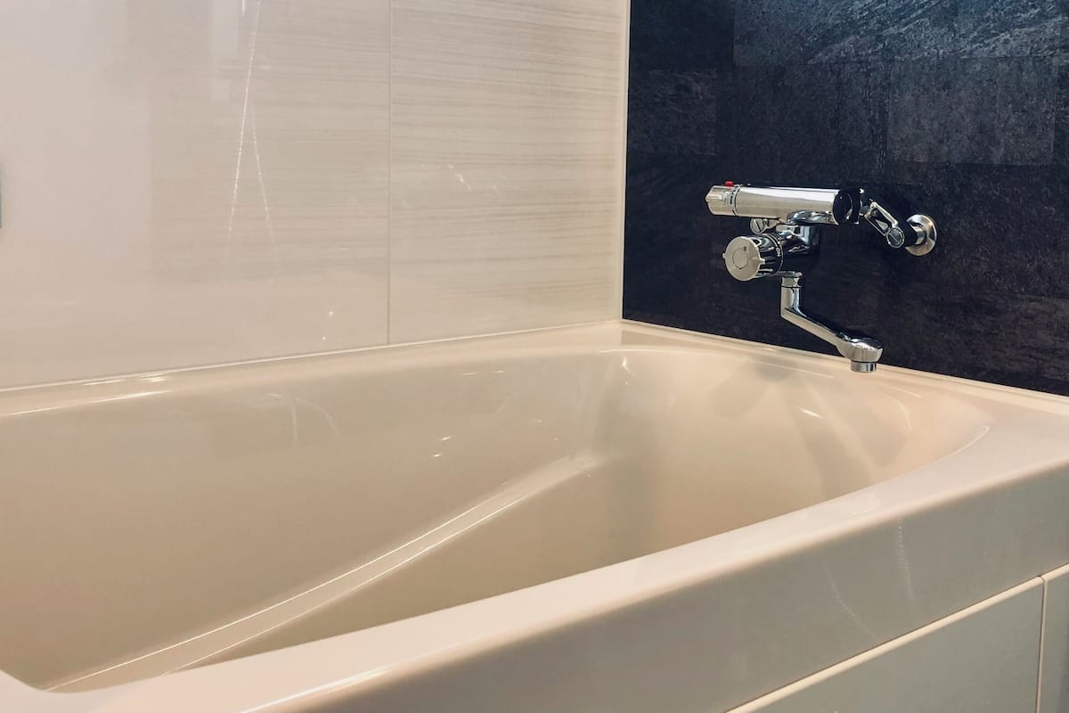 A modern bathroom with a bathtub, a wall-mounted control panel, and a dark textured wall.