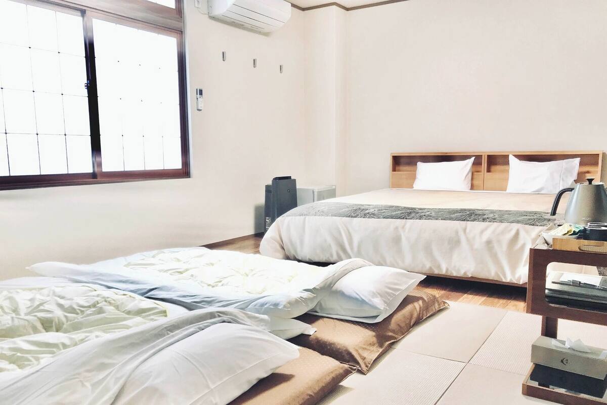 Een hotelkamer met twee bedden, een houten vloer, een raam en een nachtkastje met een lamp.