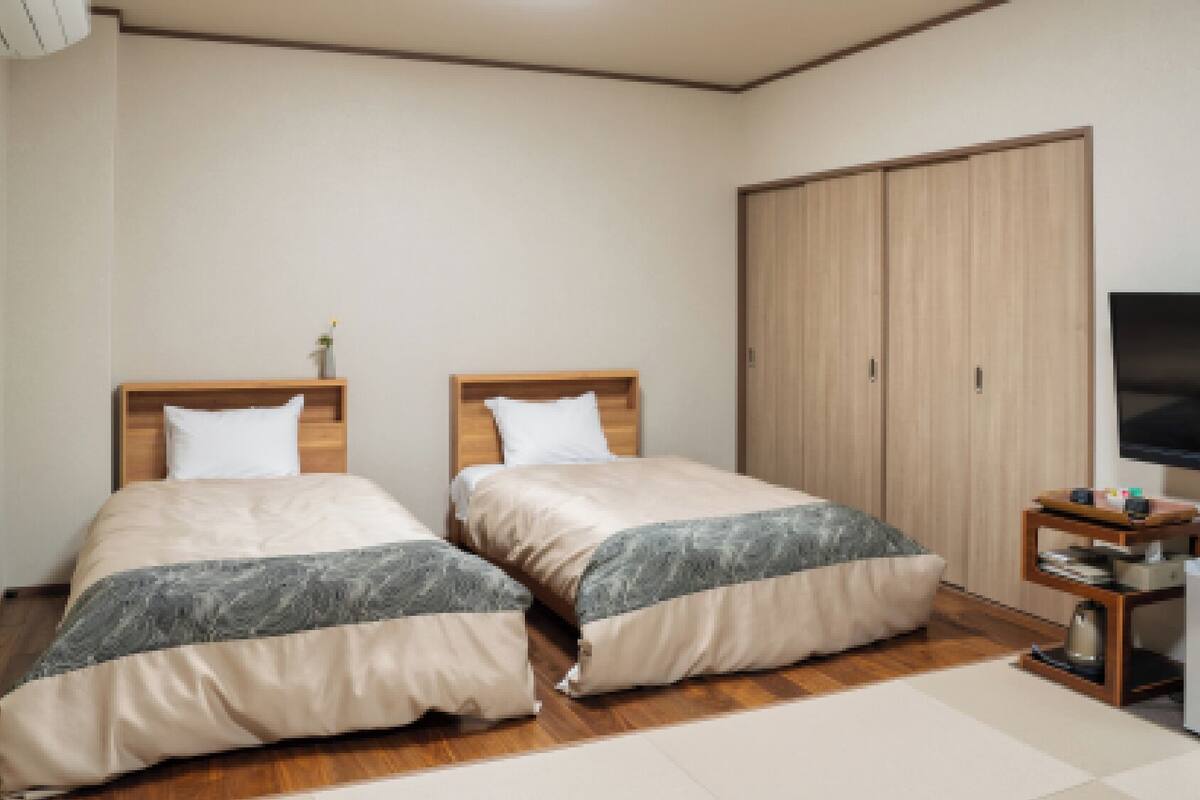 Een slaapkamer met twee bedden, een kledingkast, een televisie en een tafeltje.