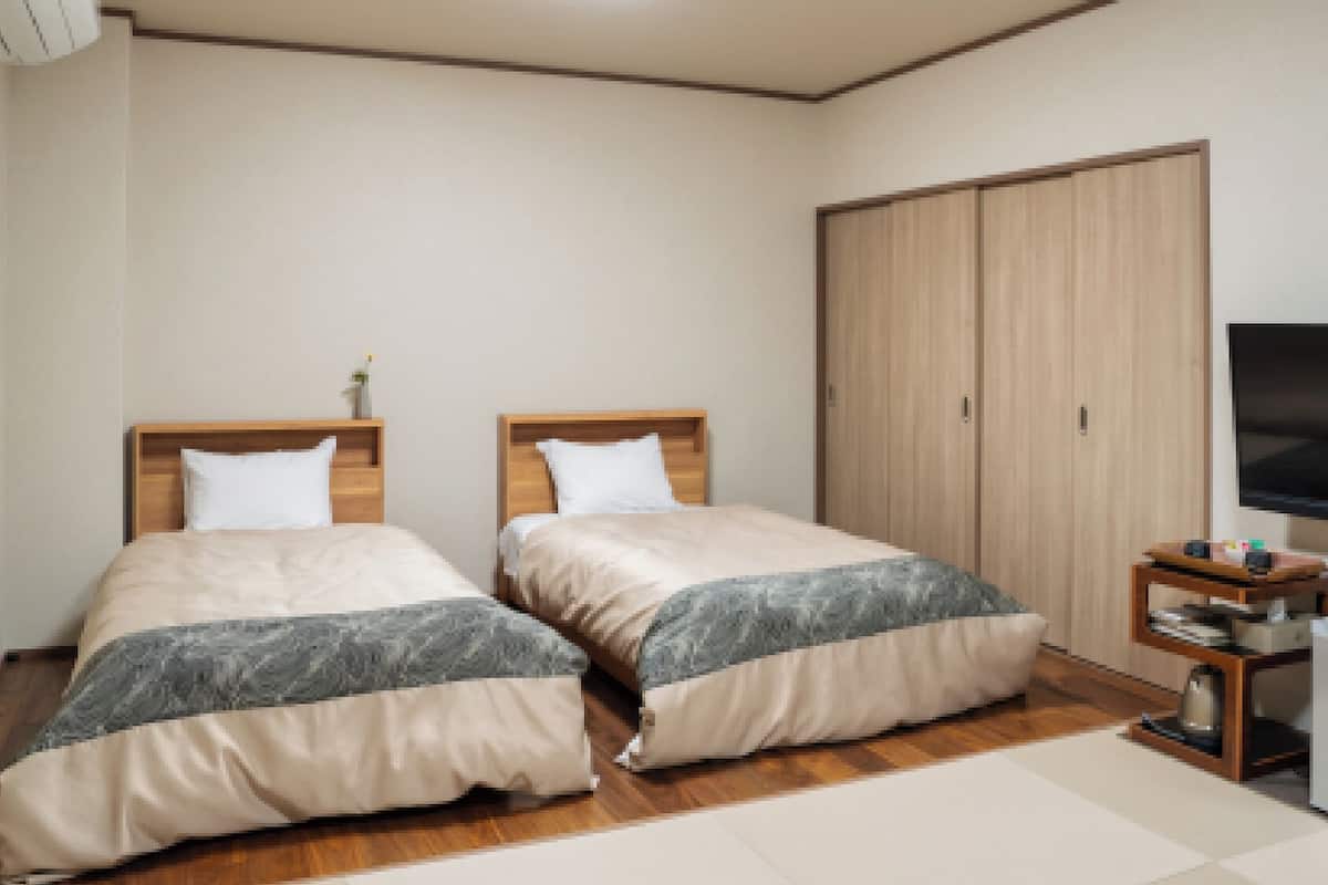 A bedroom with two beds, a wardrobe, a TV, and a small table.