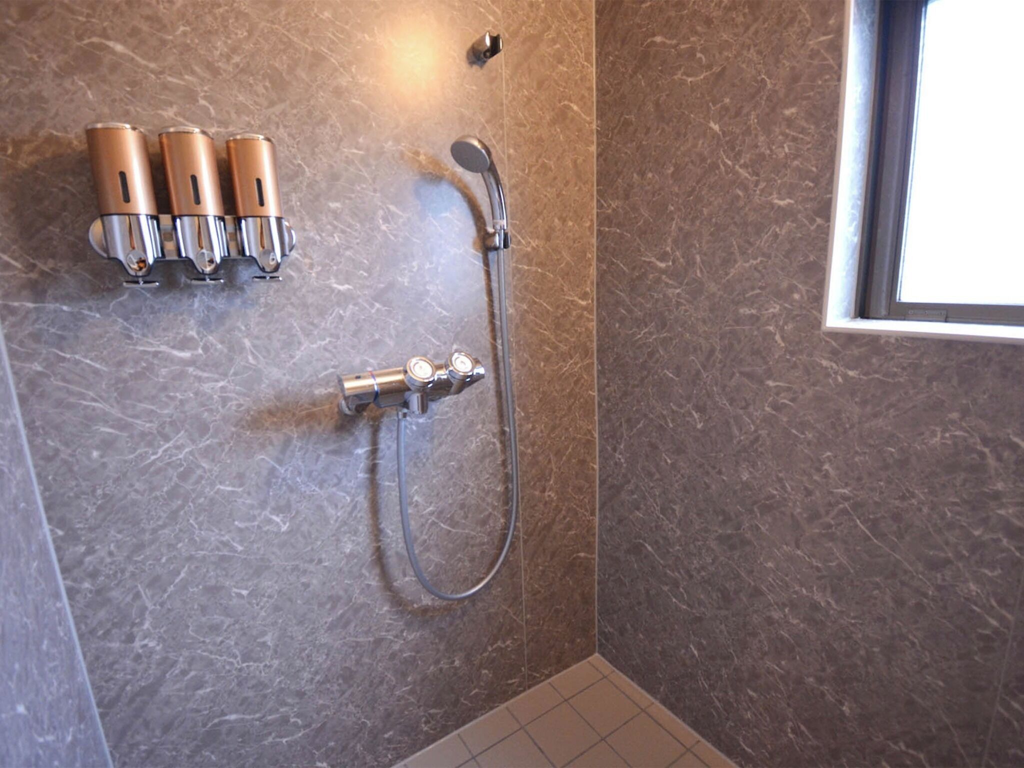 A bathroom with a shower, a towel rack with three towels, and a window.