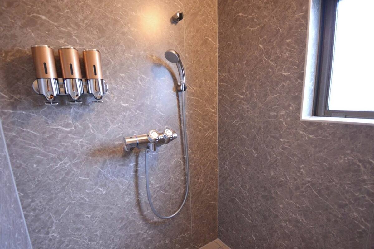 Een badkamer met een douche, een handdoekrek met drie handdoeken en een raam.