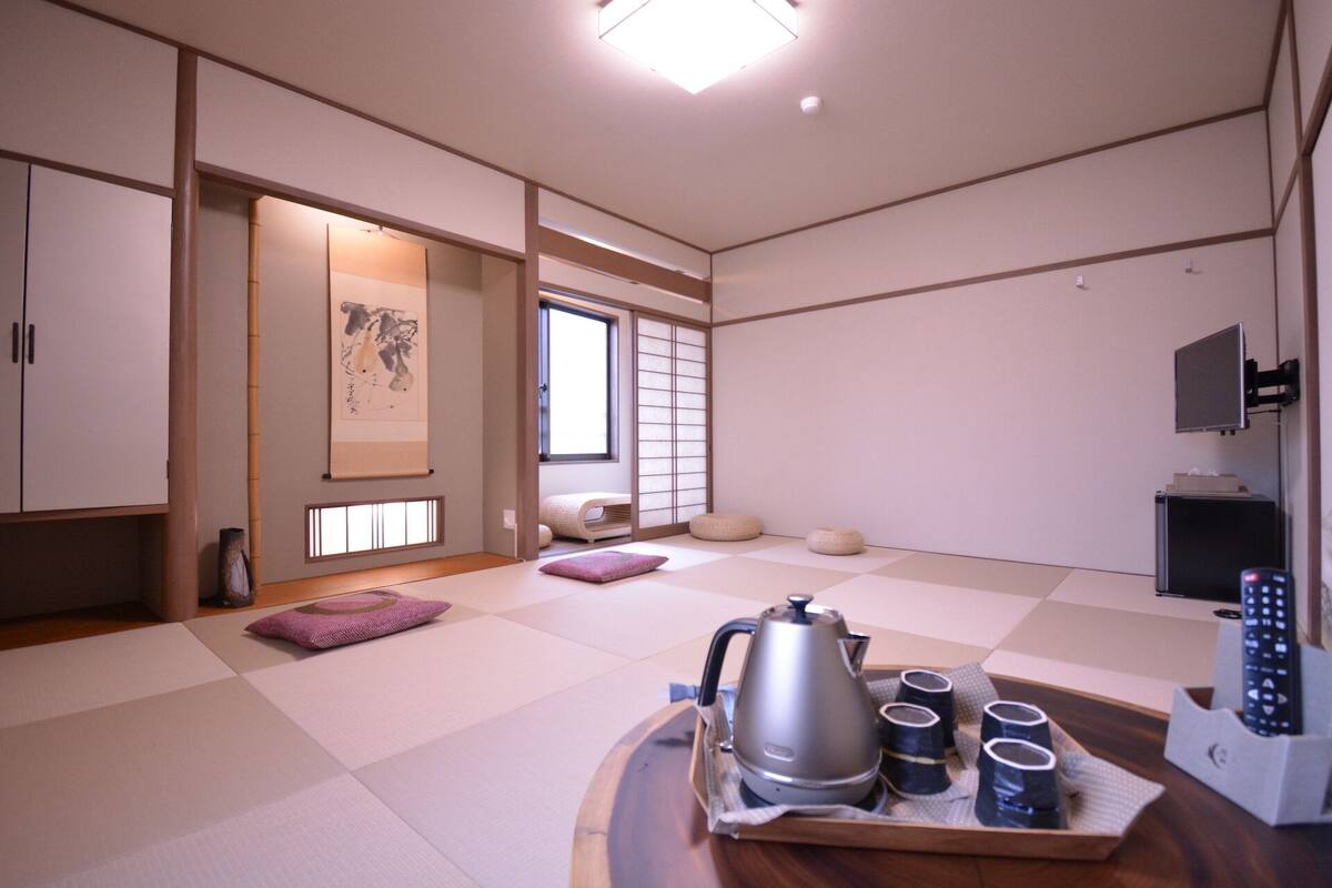 Een traditionele Japanse kamer met tatami vloeren, een tatami vloermat tafel met een waterkoker en kopjes, een schuifdeur en een televisietoestel.