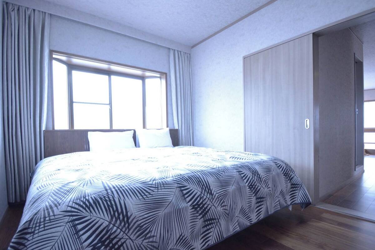 Hotelkamer met een groot bed, een raam met gordijnen, een kledingkast en een deur naar een andere kamer.