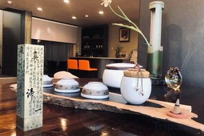 Ein traditionelles japanisches Teeset auf einem Holztisch, ergänzt durch ein Kalligraphie-Kunstwerk, ein dekoratives Glas und eine kleine Figur.