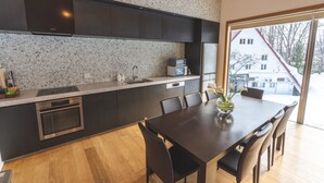 Una cocina moderna con gabinetes oscuros, encimera de granito, horno empotrado y un comedor con mesa y sillas.