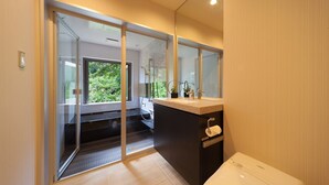 Un baño moderno con puerta de vidrio que da a la zona de ducha, un inodoro y un lavamanos con espejo.