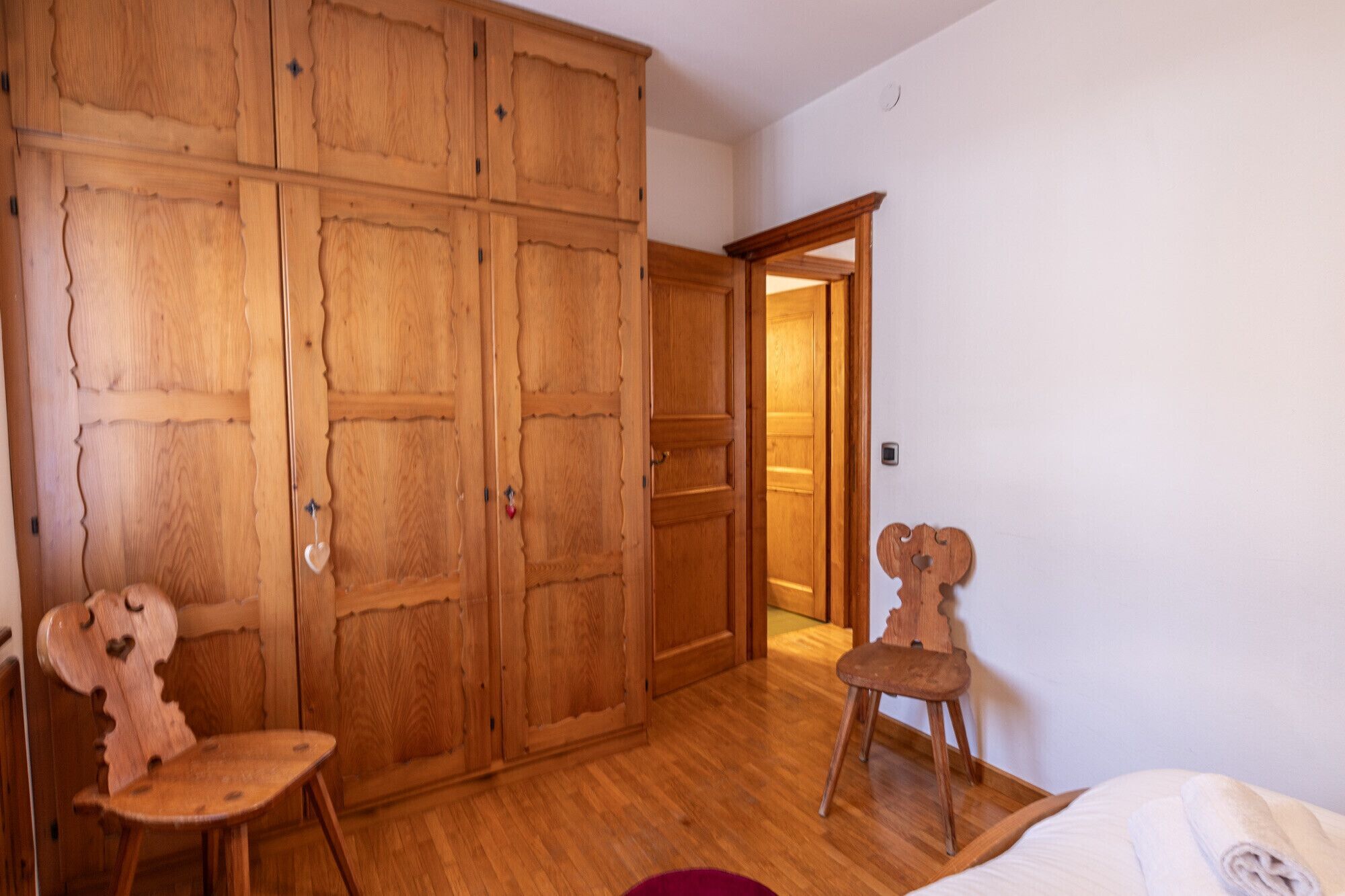 Ein Zimmer mit Holzmöbeln, darunter ein Kleiderschrank, ein Stuhl und ein Bett.