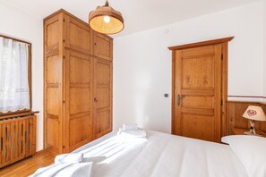 A bedroom with wooden wardrobes, a bed with white linens, a hanging lamp, and a window with lace curtains. - Casa Amalia, with panoramic terrace (Cortina d´Ampezzo)