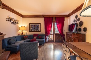 A living room with a sofa, a wooden dining table, a TV, and a painting on the wall. - Casa Amalia, with panoramic terrace (Cortina d´Ampezzo)