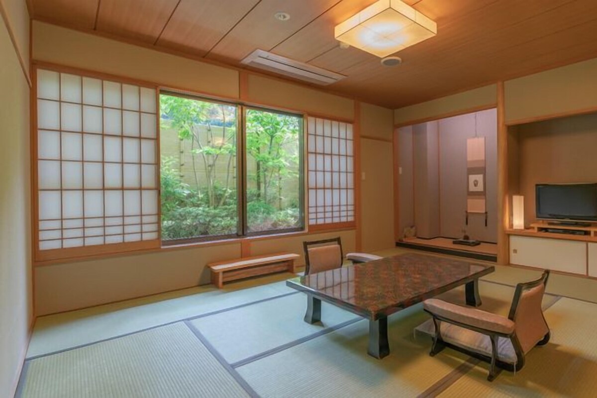 Ett traditionellt japanskt rum med tatamimattor på golvet, ett lågt bord och en tv-apparat placerad på ett träställ.