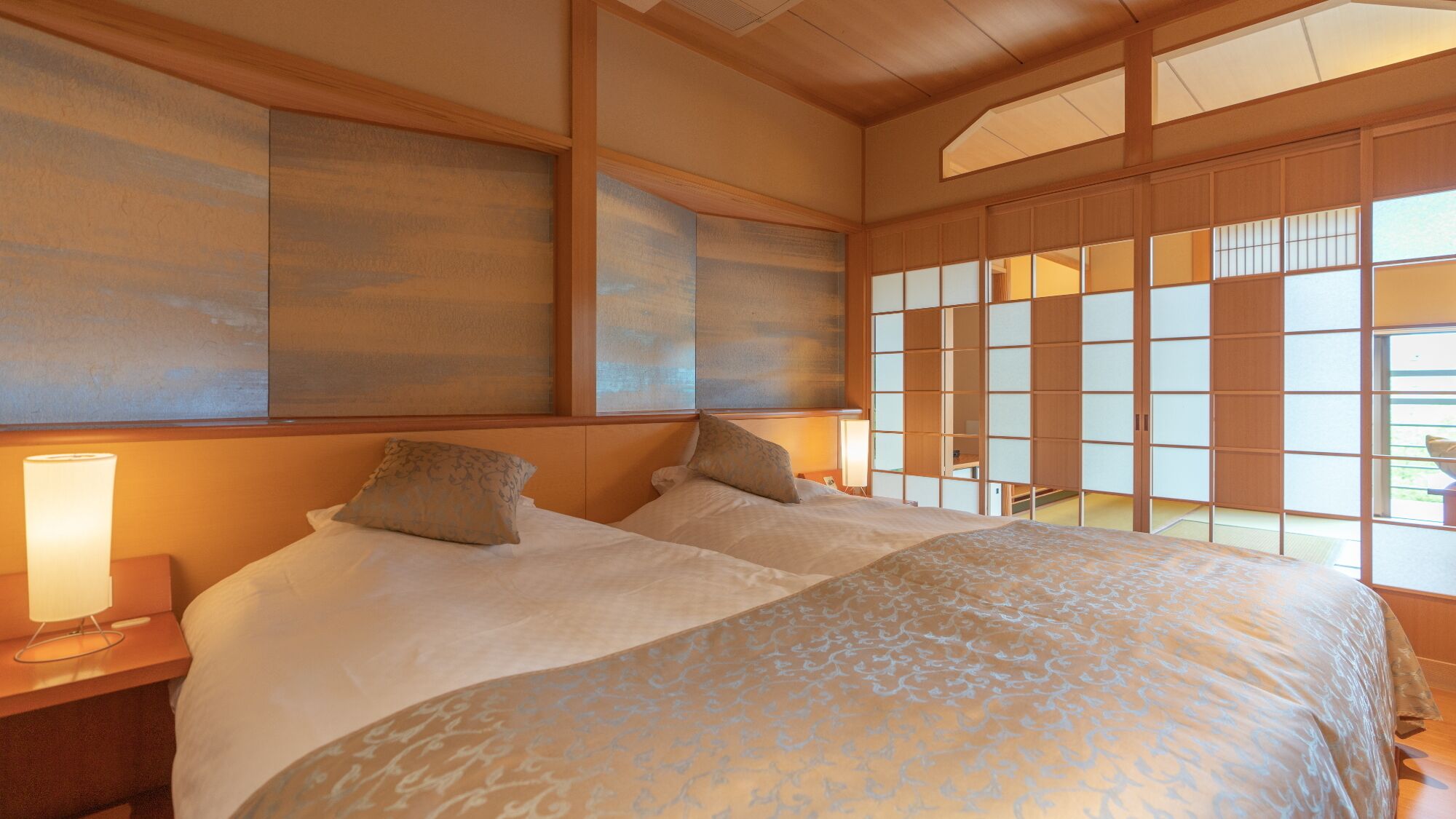 A traditional Japanese-style bedroom with tatami flooring, a large bed with patterned bedding, and sliding shoji doors.