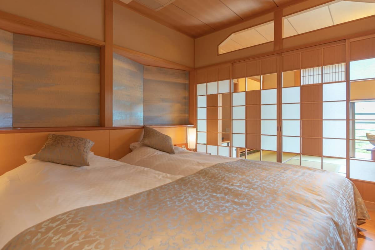 Ein traditionelles japanisches Schlafzimmer mit Tatami-Boden, einem großen Bett mit gemusterten Betttextilien und verschiebbaren Shoji-Türen.