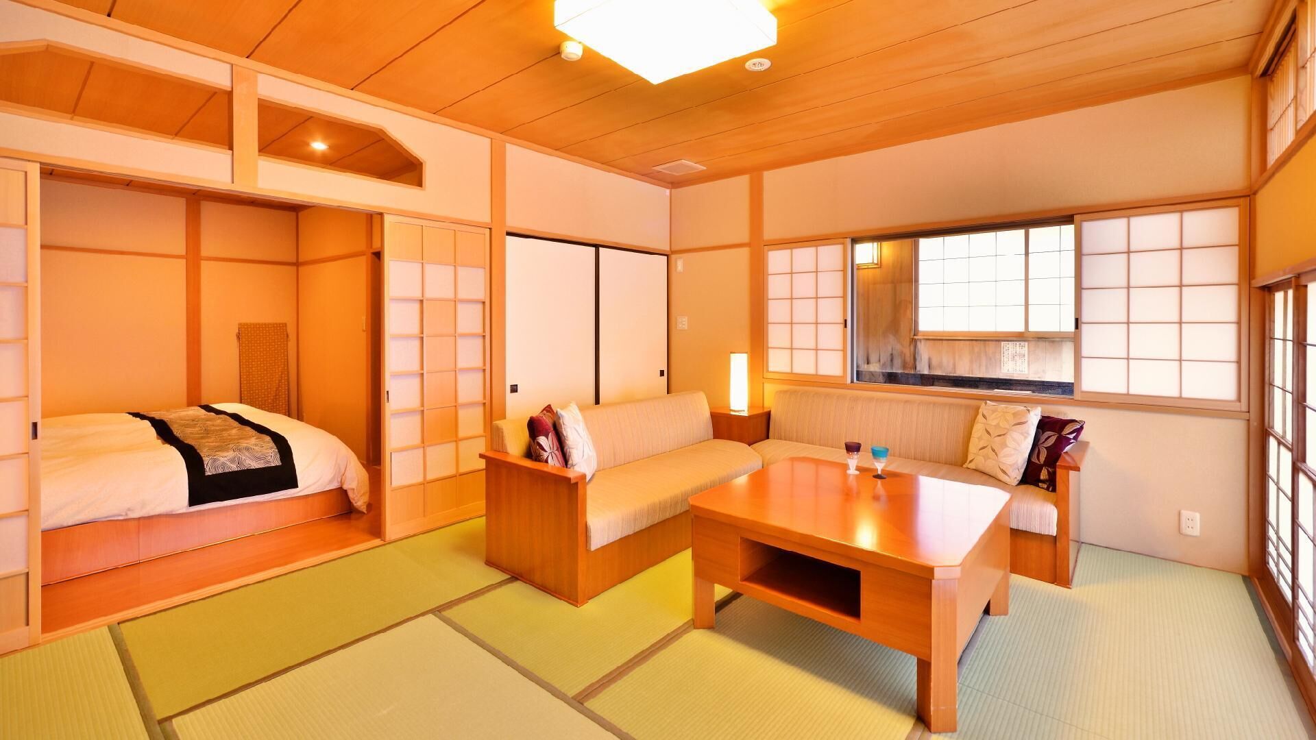 A traditional Japanese-style room with tatami flooring, a low wooden table, a sofa, and a bed with a futon.