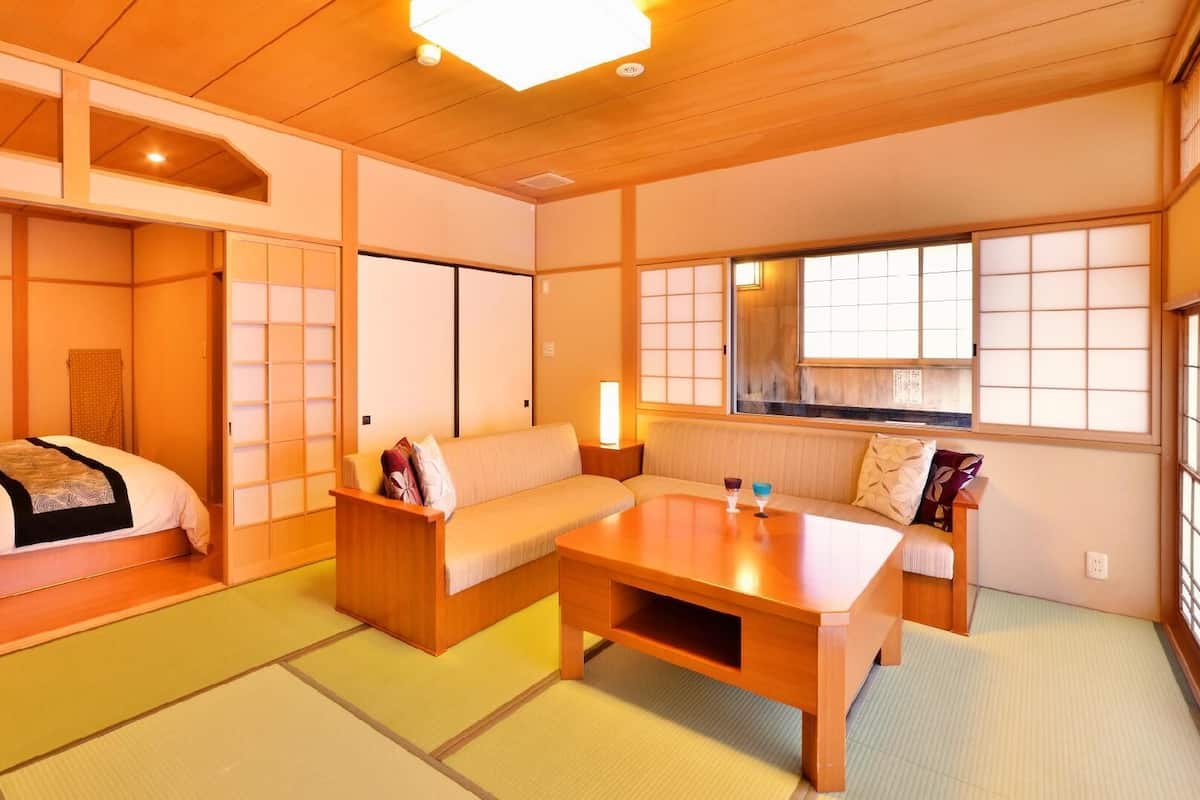 Ein traditioneller japanischer Raum mit Tatami-Böden, einem niedrigen Holztisch, einer Couch und einem Bett mit Futon.
