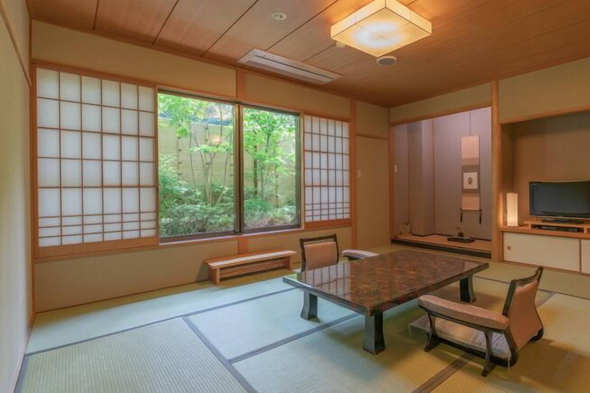 Ein traditioneller japanischer Raum mit Tatami-Bodenbelag, einem niedrigen Tisch und einem Fernseher auf einem Holzständer.
