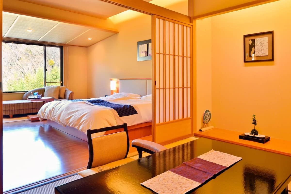 Ein traditioneller japanischer Raum mit Bett, Tisch und Blick auf Bäume.