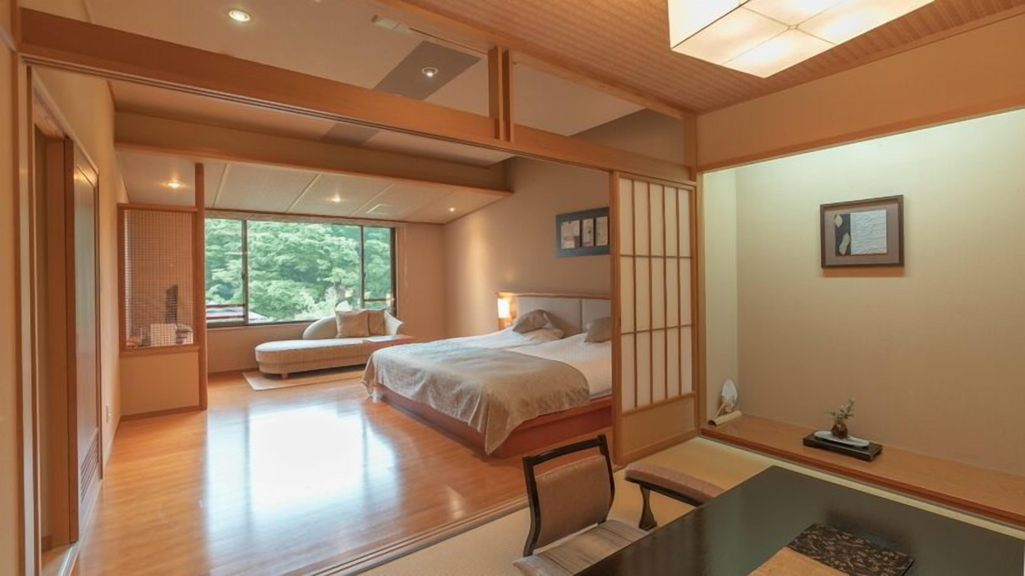 A spacious bedroom with a large bed, a desk, and a view of greenery outside.