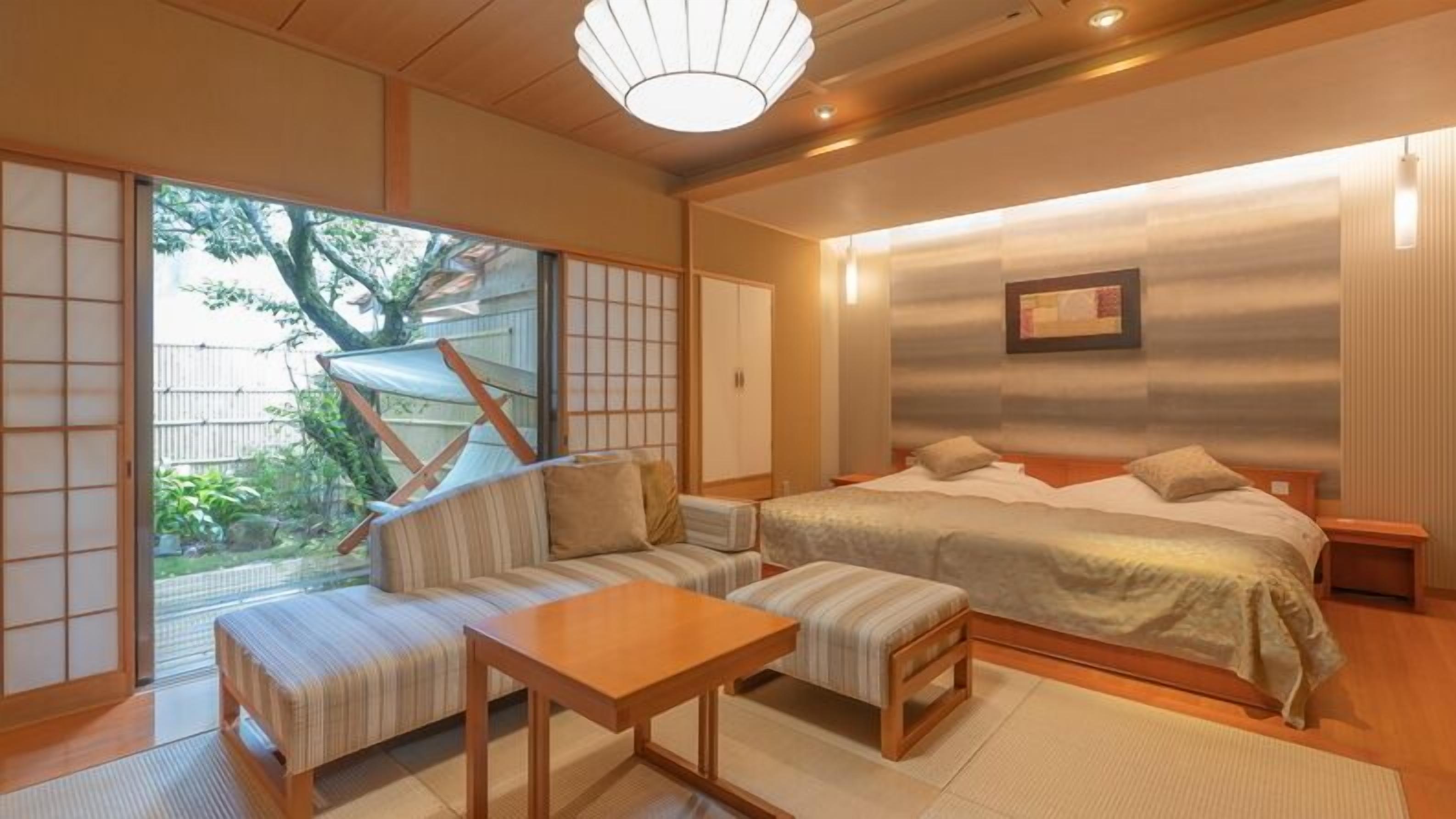A traditional Japanese-style bedroom with tatami flooring, a low table, a sofa, and a bed.