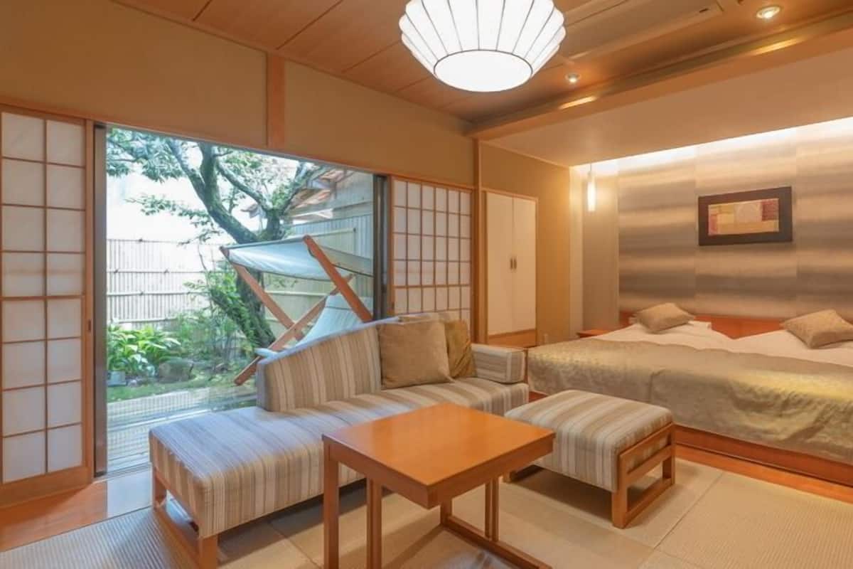 Ein traditionelles japanisches Schlafzimmer mit Tatami-Bodenbelag, einem niedrigen Tisch, einer Couch und einem Bett.