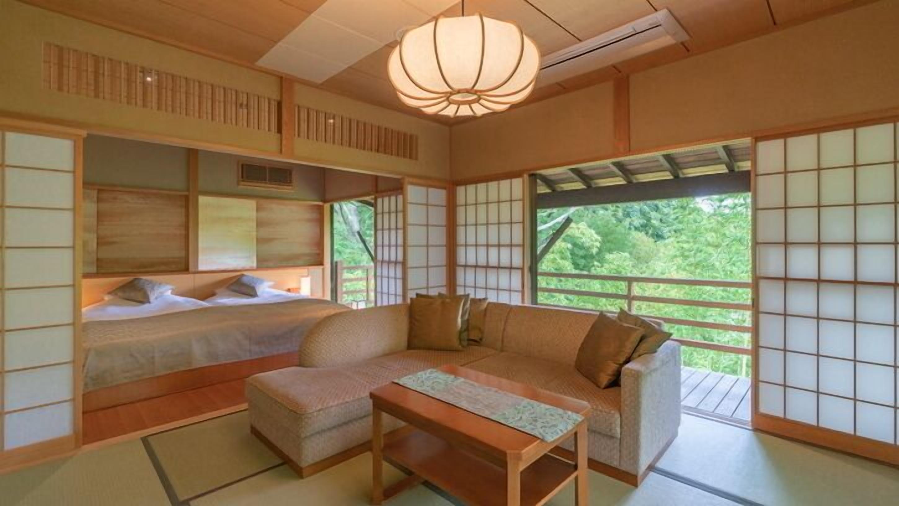 A traditional Japanese-style room with tatami flooring, a low table, a sofa, and a bed with a view of greenery outside.