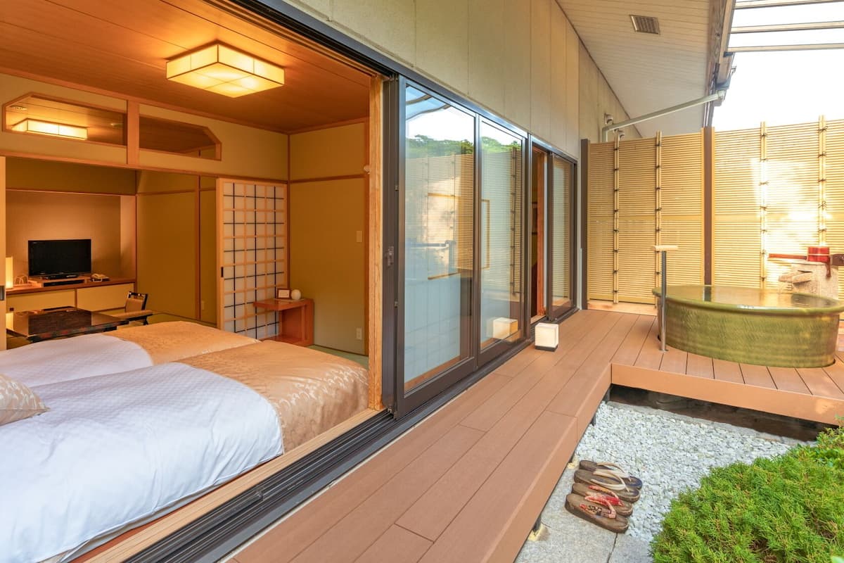 Ein traditioneller japanischer Raum mit Tatami-Boden, Futon-Bett, Schiebetüren und einer Onsen-Badewanne.