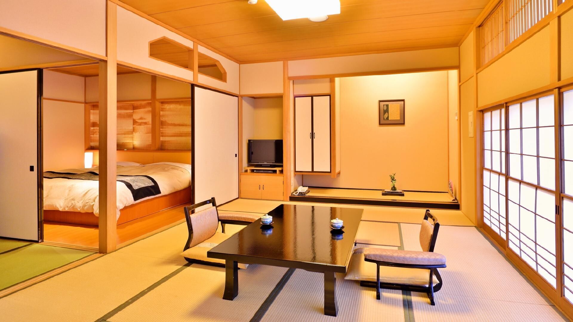 A traditional Japanese-style room with tatami flooring, a low table, a bed, and sliding doors.